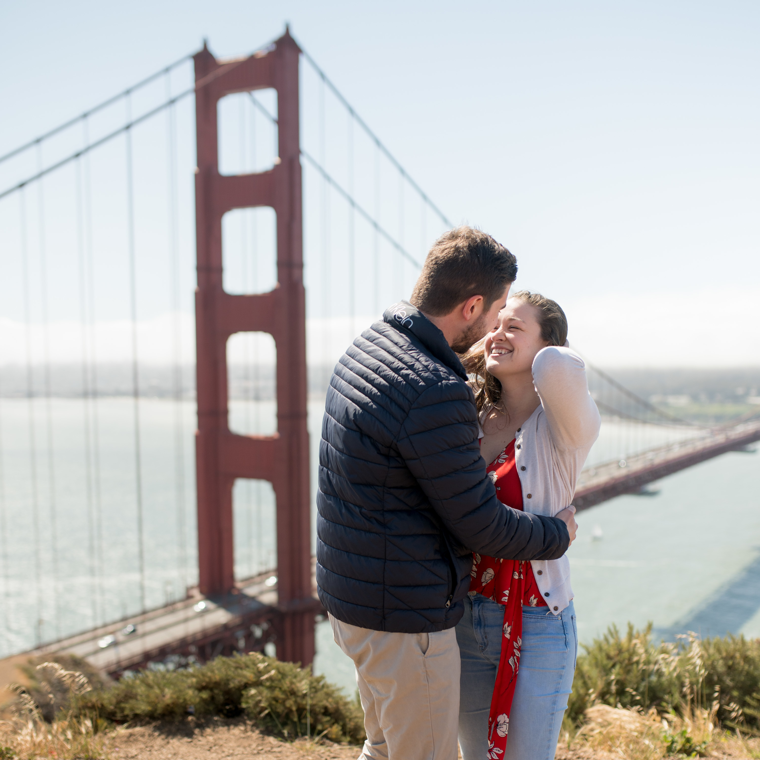 Happy couple right after a proposal at Battery Spencer with Golden Gate Bridge softly in the background